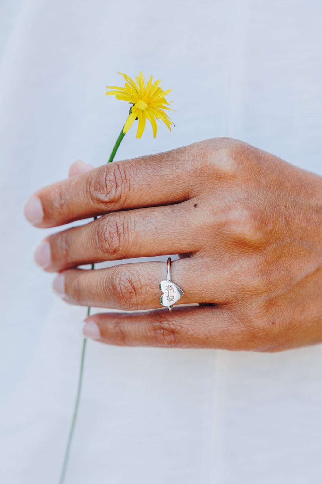simple silver heart bahai ringstone ring holding yellow dandelion flower