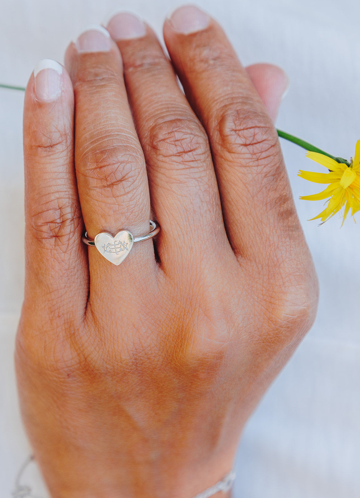 simple silver heart bahai ringstone ring holding yellow dandelion flower