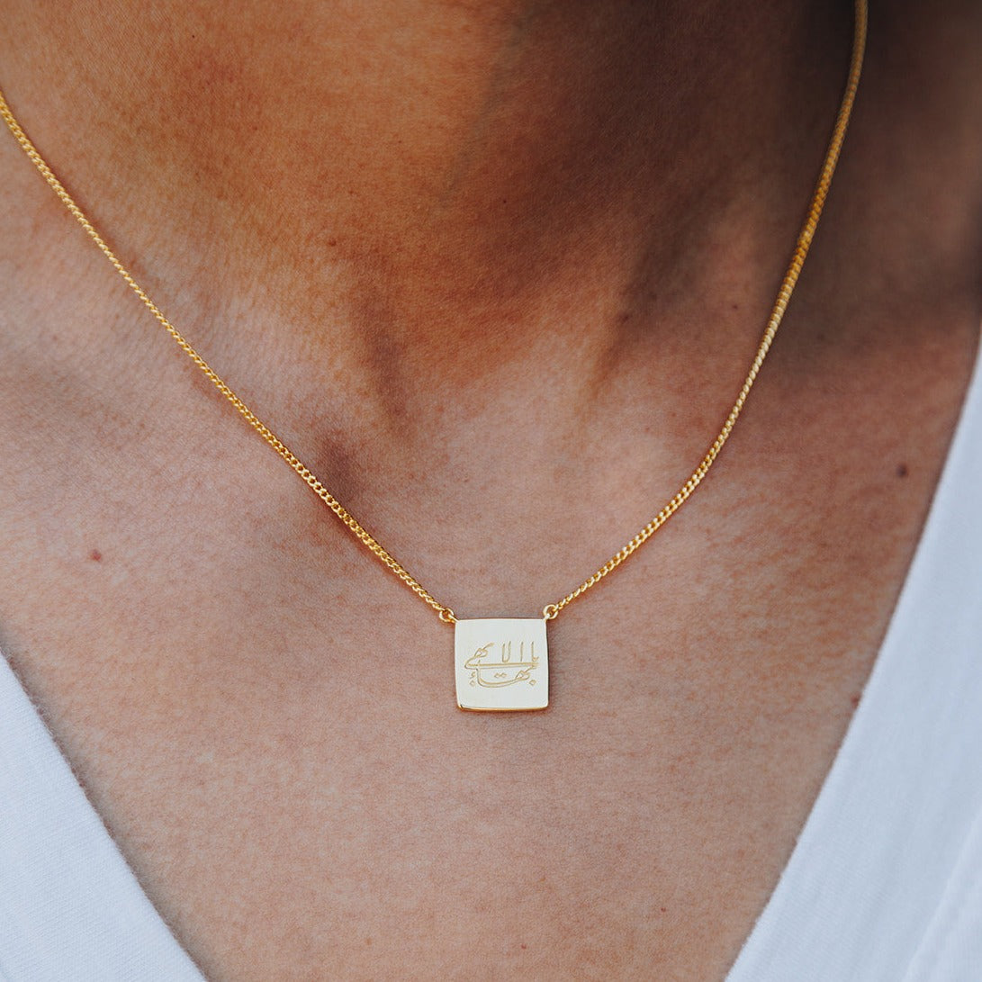 simple gold cushion Baha'i necklace with an engraving of the Greatest Name in Arabic