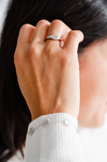plain and simple silver bahai ring with ringstone symbol engraved on a horizontal oval signet ring on an asian women's right ring finger brushing back her straight black hair 