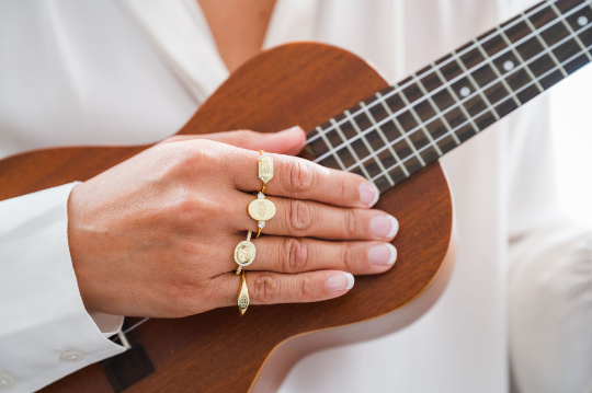 gold bahai ringstone symbol rings on each finger of an asian women's right hand holding a wooden ukulele for size and style comparison